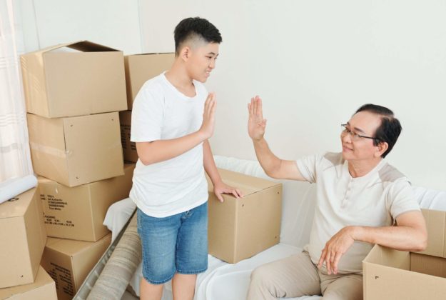 Teenage boy giving his grandfather high five after packing all belongings in cardboard boxes