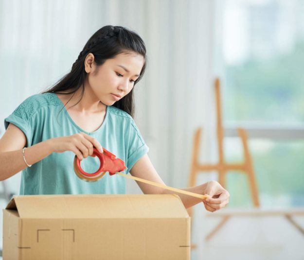 Asian young woman packing the cardboard box with adhesive tape she moving the new house